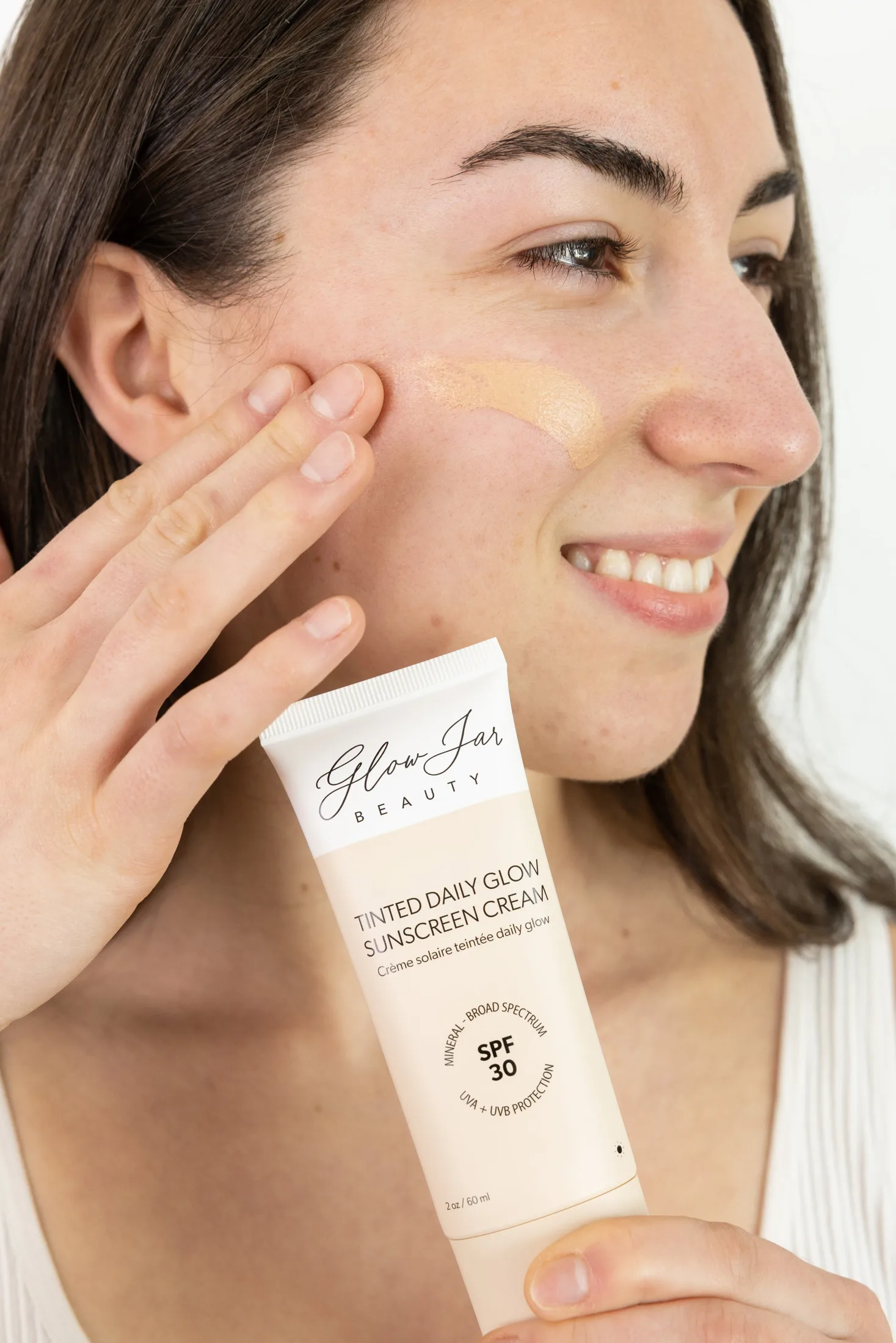 A woman smiling as she applies Glow Jar Beauty Tinted SPF 30